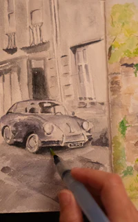 a person is drawing a car in a watercolor sketchbook